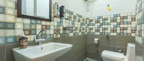 A bathroom with a sink, toilet, and a mirror. The walls are tiled with a mosaic pattern.
