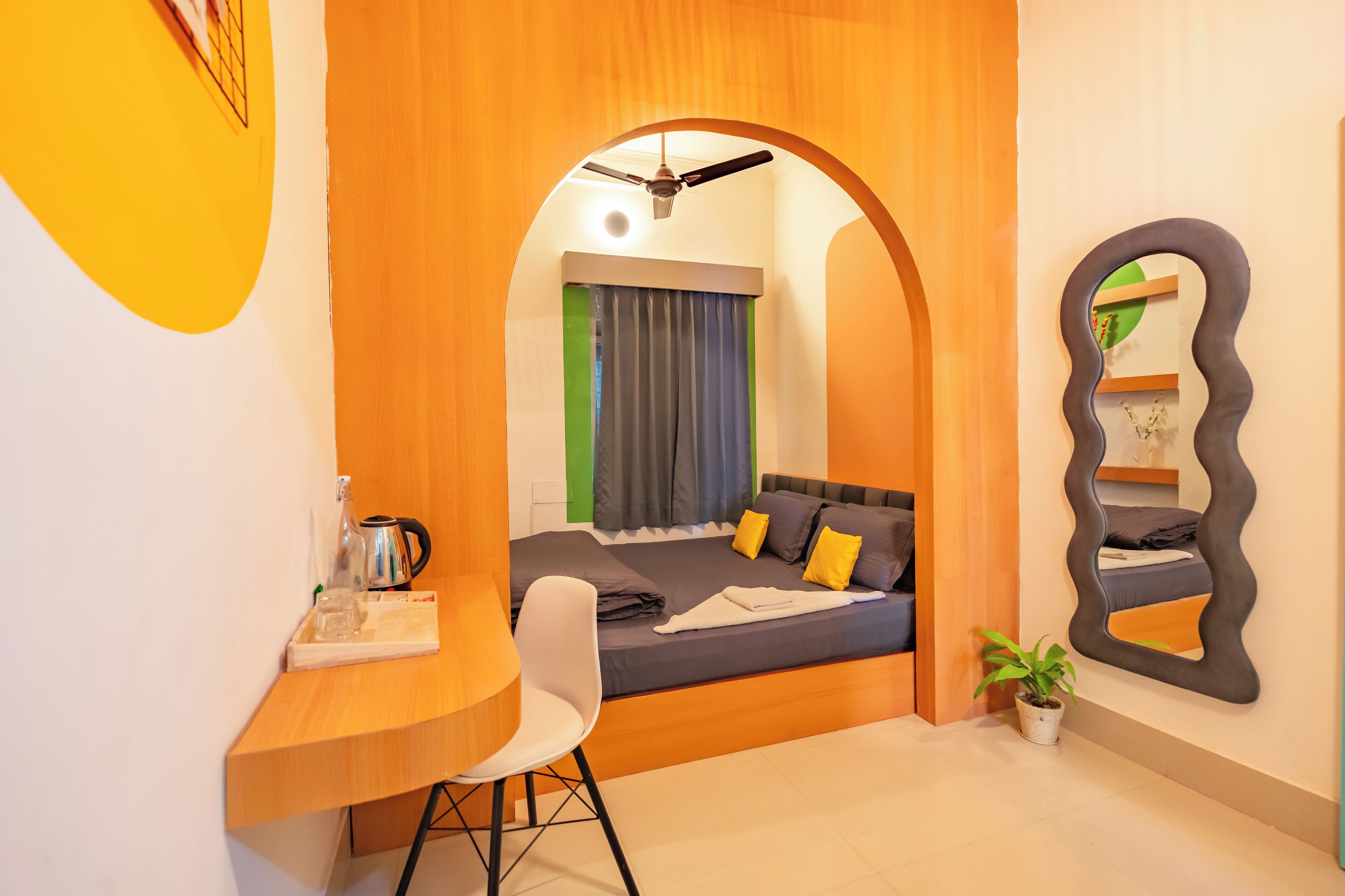 Una habitación compacta con cama, escritorio, silla, ventilador de techo y espejo.