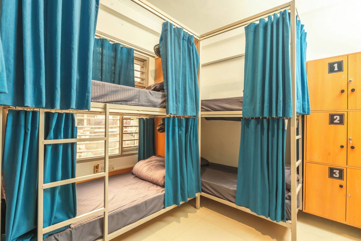 Une chambre avec un lit superposé, des rideaux, une fenêtre et une armoire en bois dotée de compartiments numérotés.
