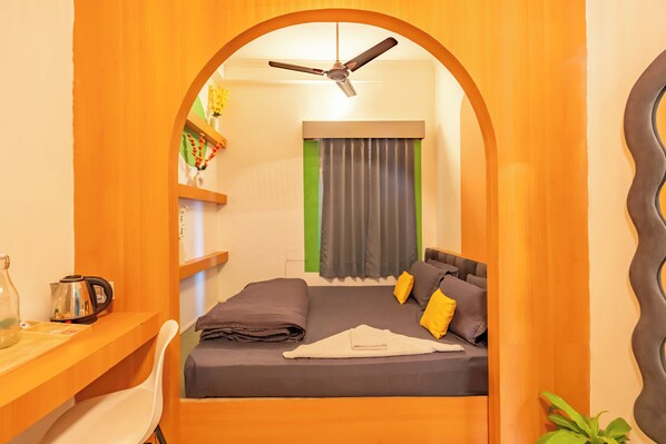 A compact hotel room with a bed, a desk, a ceiling fan, and a window with curtains. - Hostel De Offlanders Rishikesh • Stay • Connect • Explore (Rishikesh)
