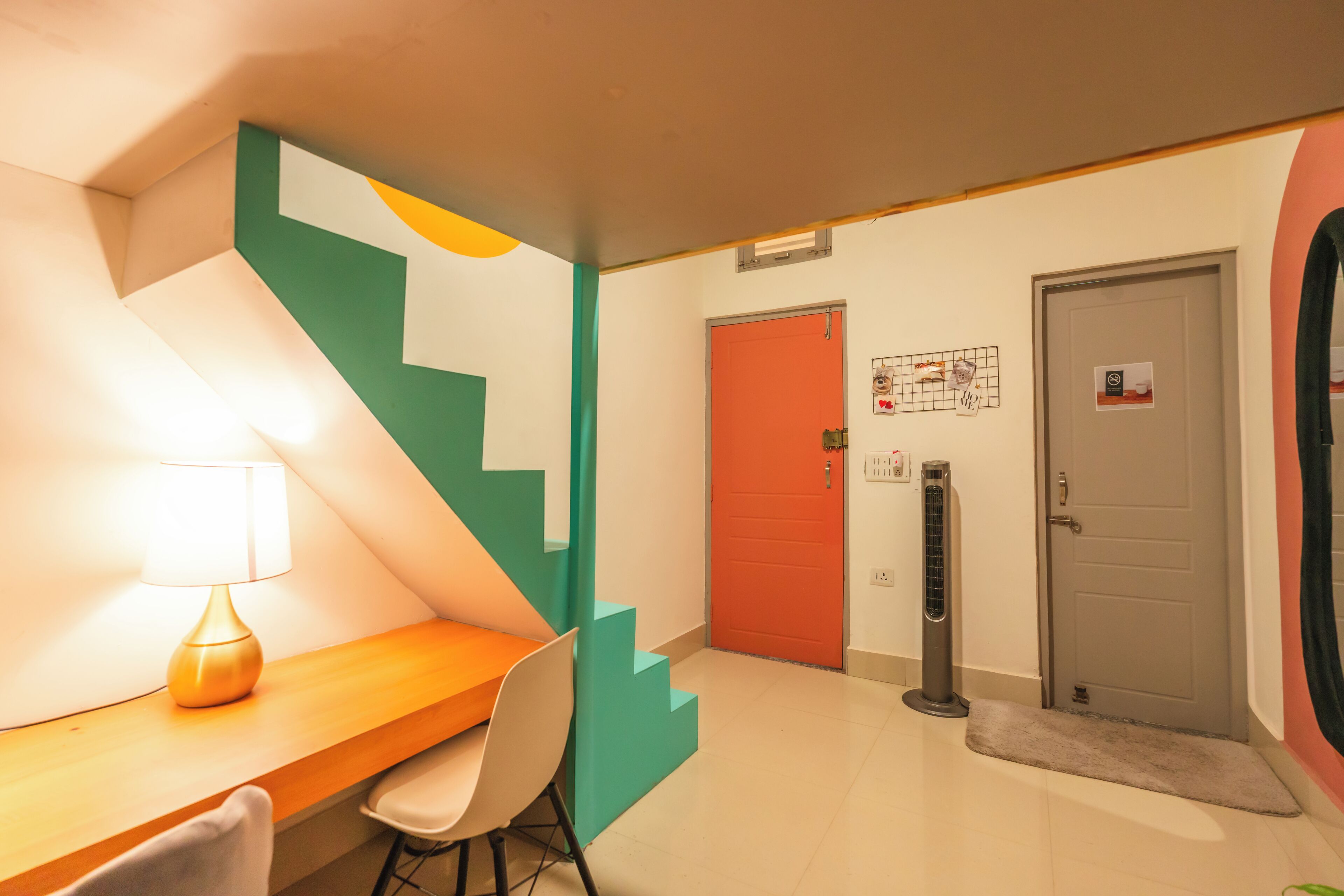Un hall d’hôtel moderne avec un bureau en bois, une chaise, un escalier aux marches de couleur turquoise et une porte rouge.