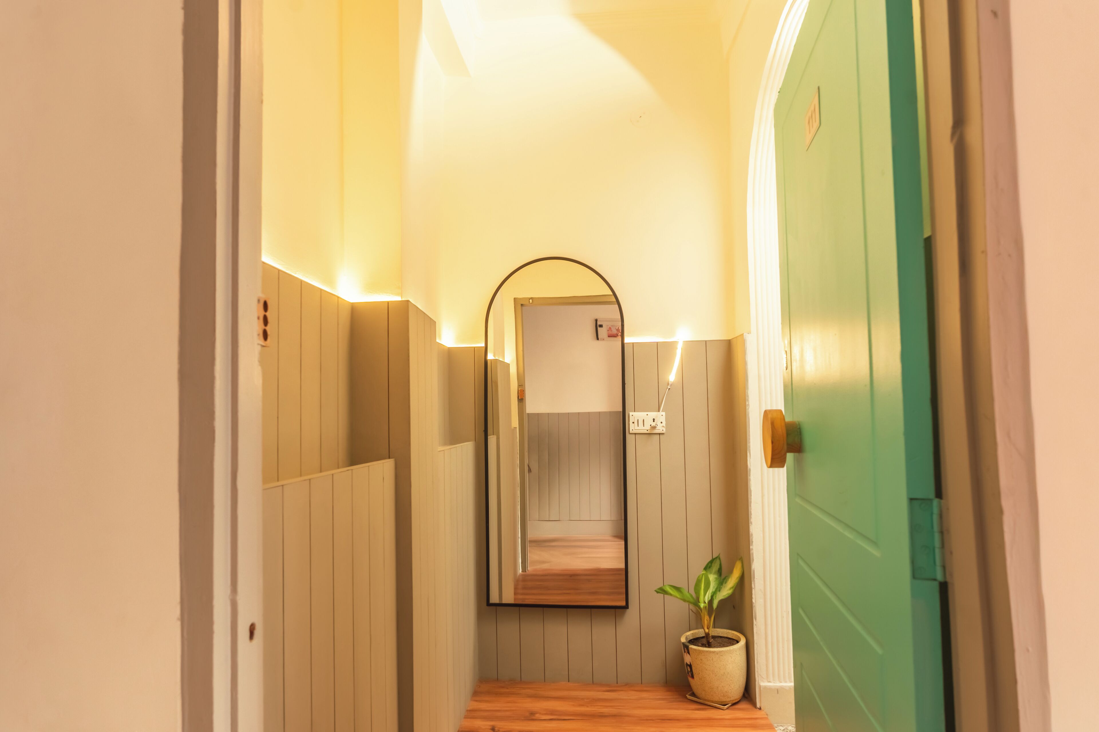 A narrow hallway with wooden paneling, a green door, and a potted plant.