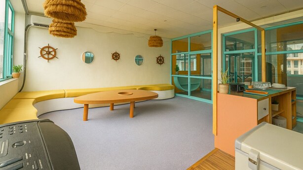 A room with a curved bench, a round table, and a desk with a computer. There are nautical-themed wall decorations and a large window. - Hostel De Offlanders Rishikesh • Stay • Connect • Explore (Rishikesh)