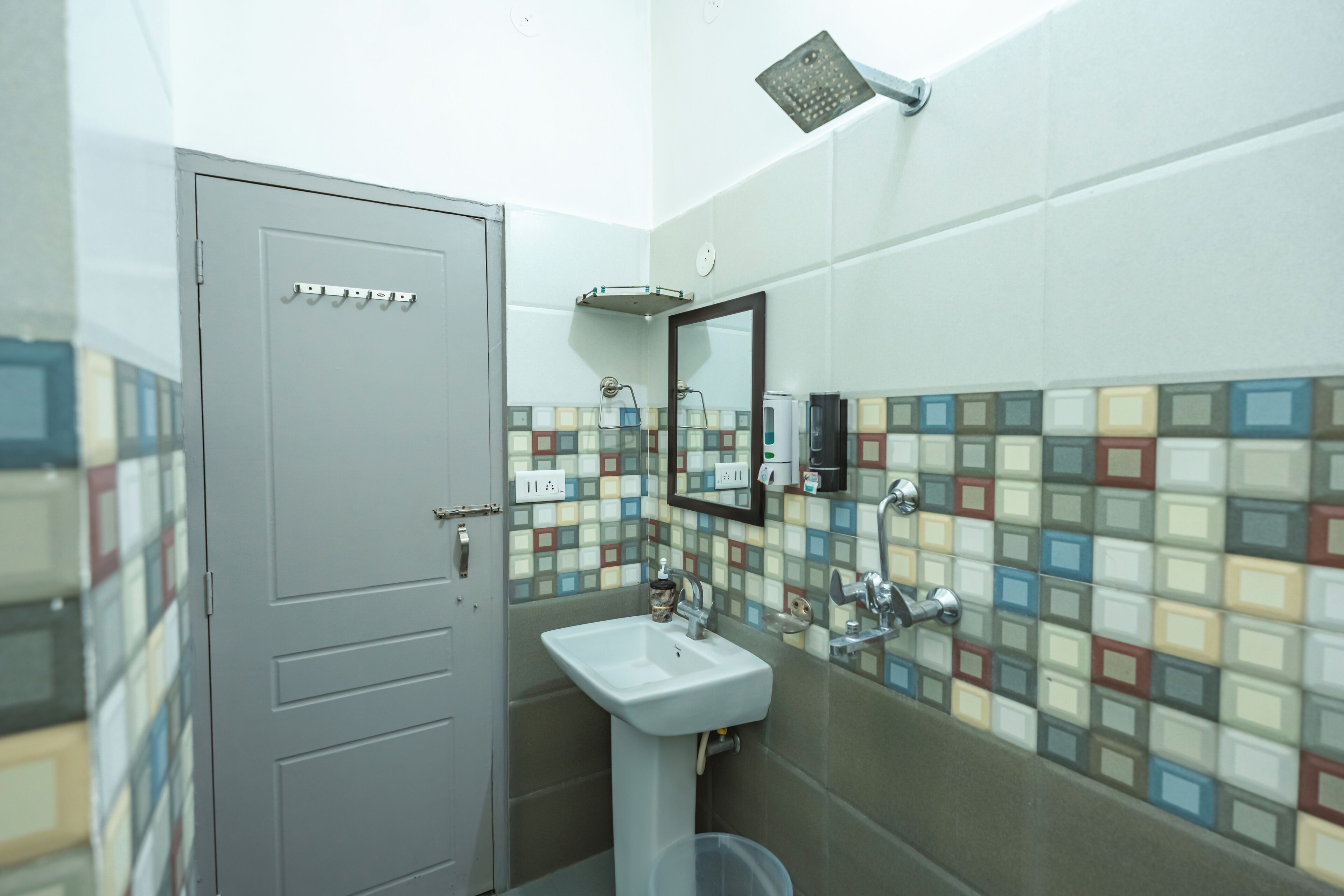 A bathroom with a tiled wall, a sink, a mirror, and a shower.