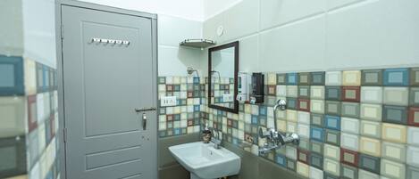 A bathroom with a tiled wall, a sink, a mirror, and a shower.