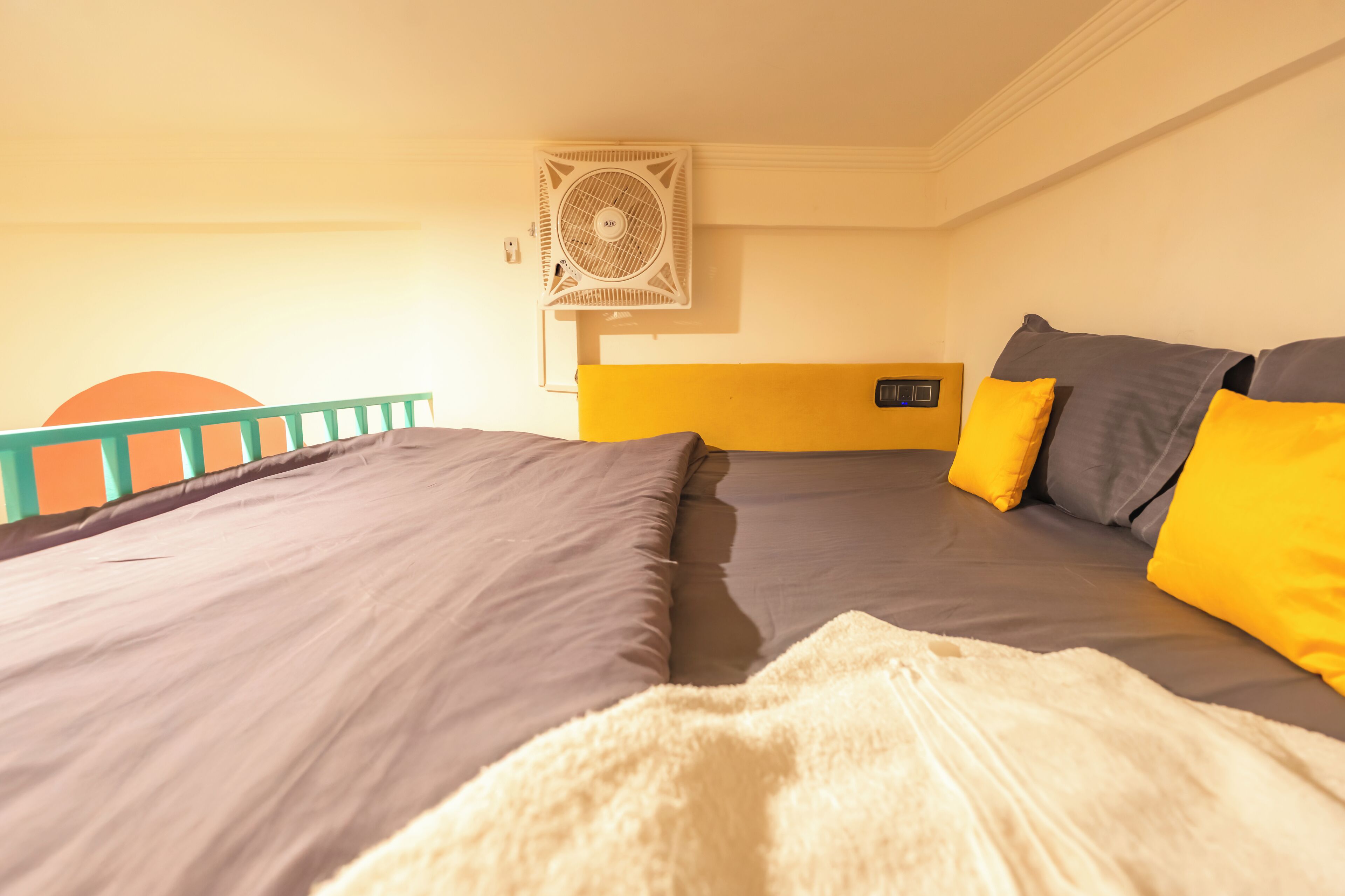A room with two beds, each with a grey mattress and yellow pillows. There is a white air conditioning unit on the wall.