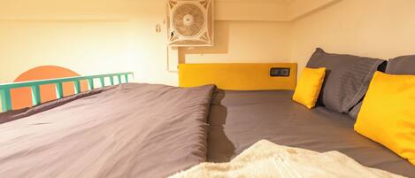 Una habitación con dos camas, cada una con colchón gris y almohadas amarillas. Hay un equipo de aire acondicionado blanco en la pared.