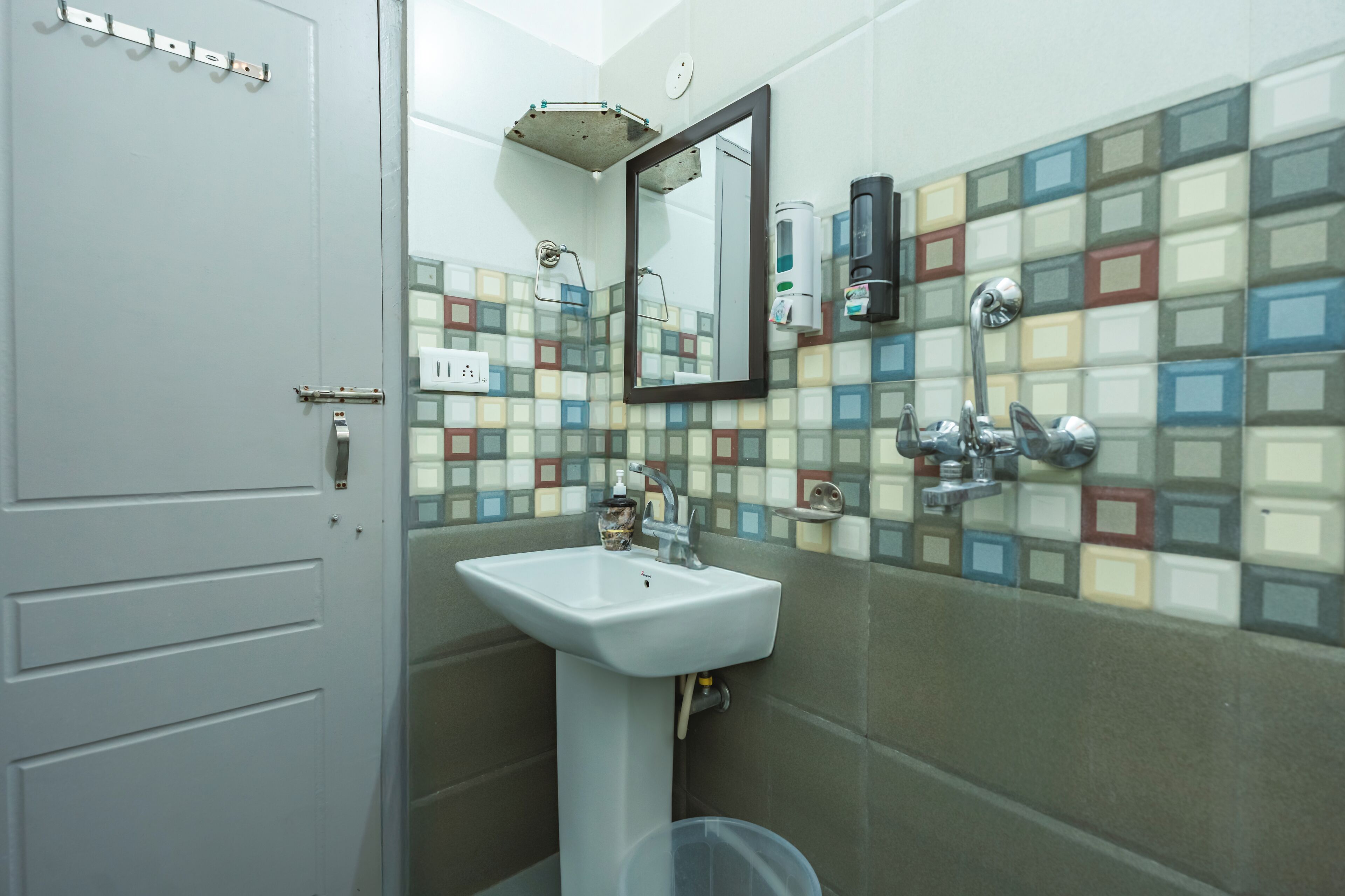 A bathroom with a white sink, a mirror, a shower, and a tiled wall with a multicolored pattern.