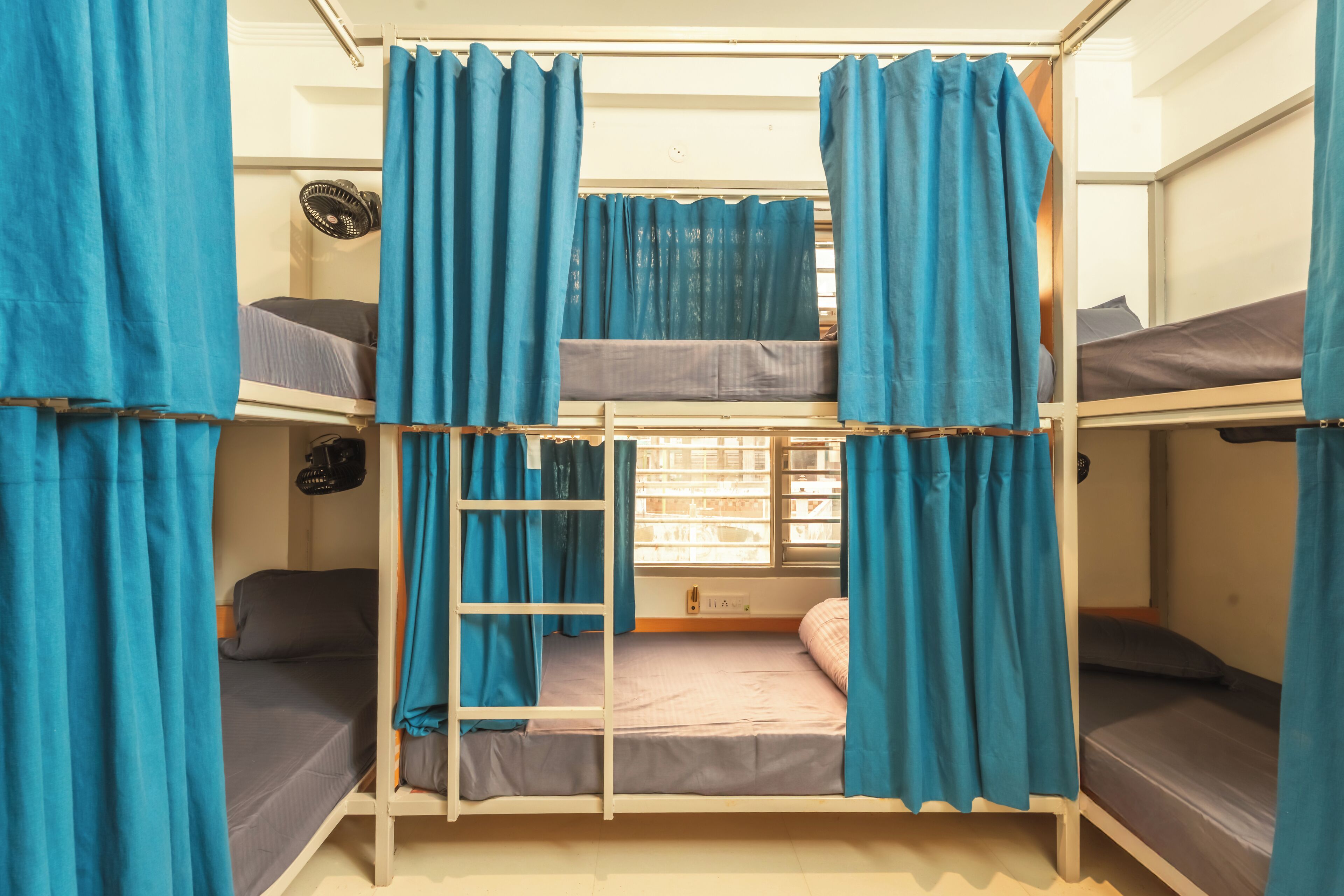 Quarto com beliche, cortinas azuis, escada e janela com persianas.