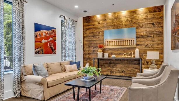 A living room with a beige sofa, a coffee table, and a patterned rug. There is a wooden wall with a painting and a shelf with decorative items. - Neon Daes Amazing Location Near Vandy & Centennial Park, 10 min to Broadway (Nashville)