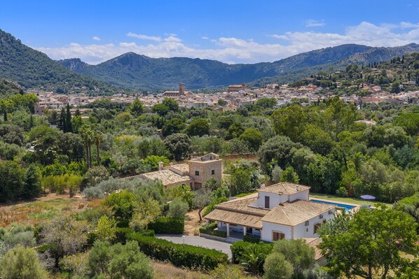 A villa with a tiled roof, surrounded by lush greenery and a mountainous backdrop.