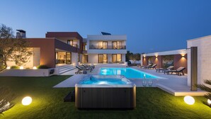 Una casa moderna con piscina, jacuzzi y mobiliario de exterior.