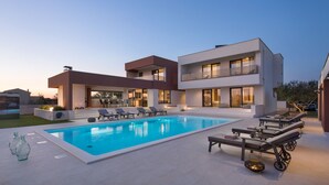 Una casa moderna de dos pisos con piscina, zona de estar al aire libre y un patio bien iluminado.