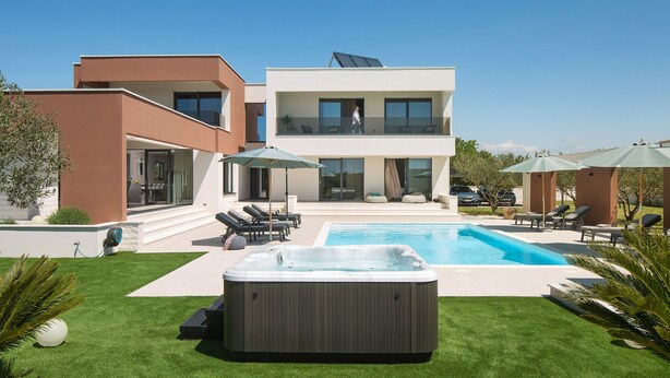 Una casa moderna de dos pisos con piscina, jacuzzi y mobiliario de exterior.