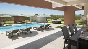 Un área junto a la piscina con sillones, sombrillas y una mesa de comedor.