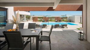 Zona junto a la piscina con mesa, sillas y sombrillas.