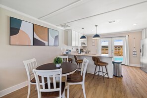 A modern kitchen with white cabinetry, a dining area with white chairs, a small potted plant, and a view of a pool through the window.