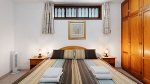 A bedroom with a bed, two bedside tables, a window with curtains, a wooden wardrobe, and a framed picture on the wall.