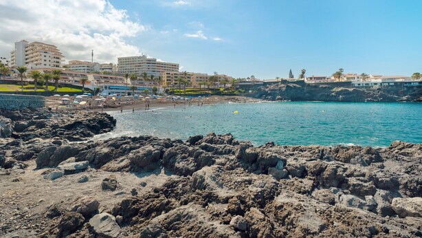 A coastal beach with rocky terrain, a sandy beach, and buildings in the background.