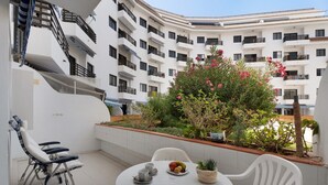A balcony with a white table, chairs, and a fruit bowl.