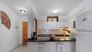 A modern kitchen with white cabinets, a black countertop, and two white bar stools.