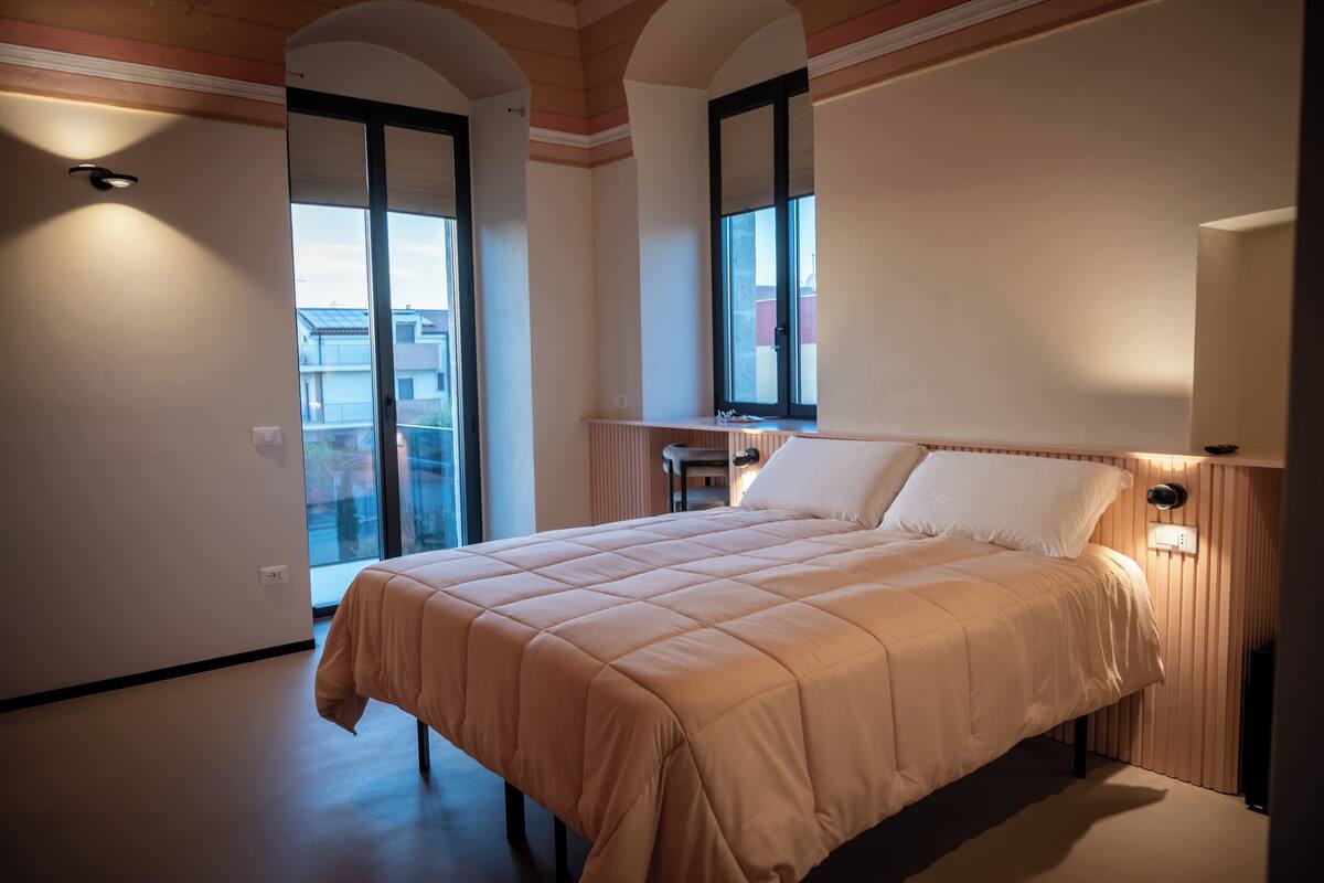Un dormitorio con una cama grande, una ventana y una puerta que da a un balcón.