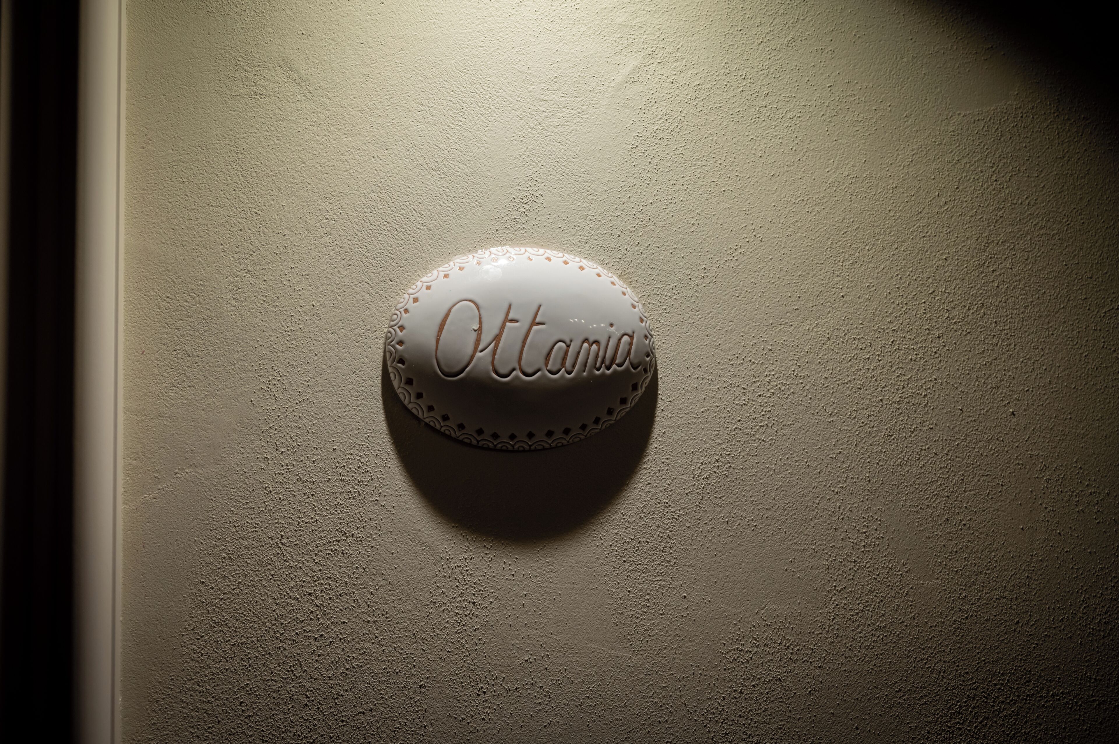 A textured wall with a round, white sign that reads "Ottania."
