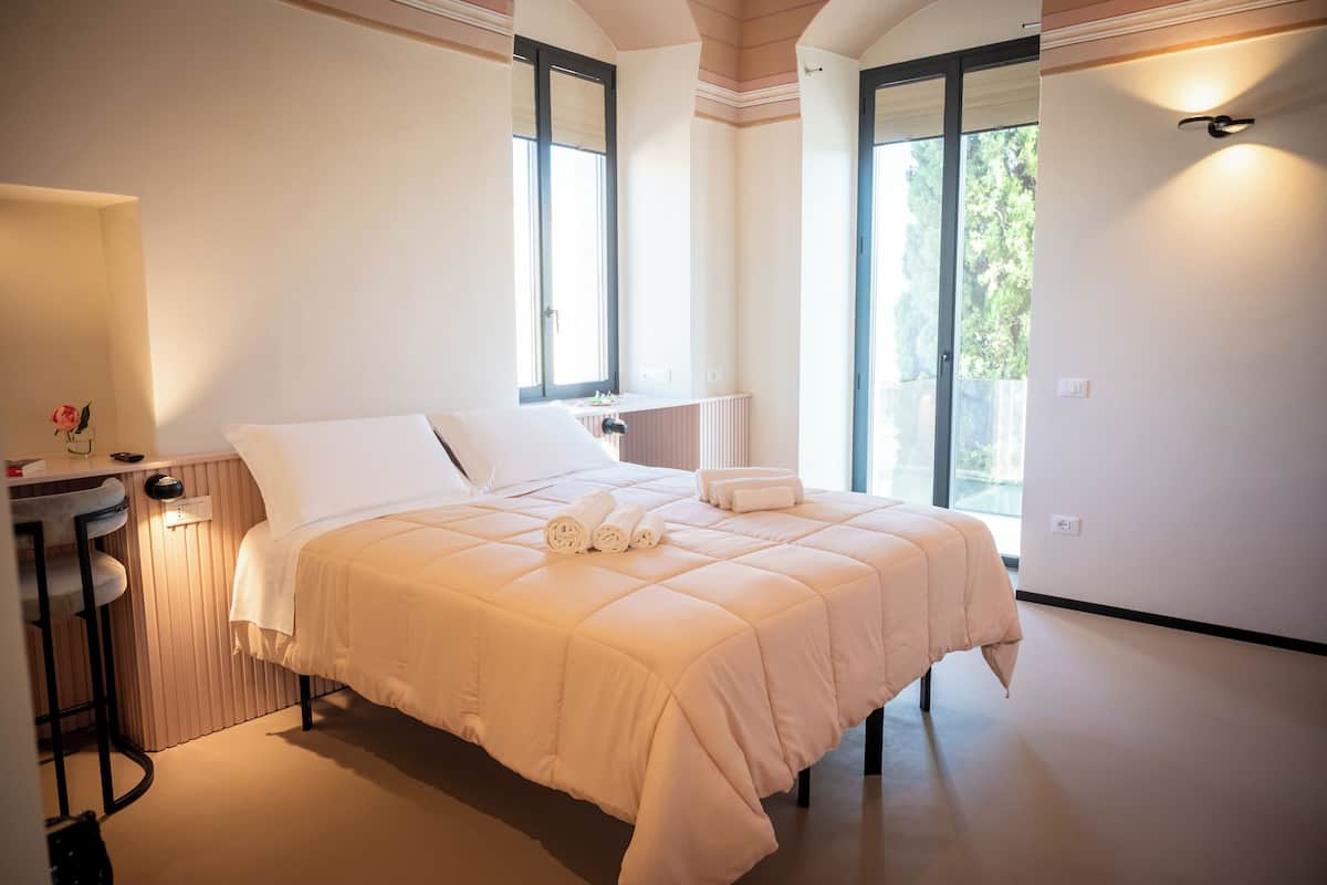 Un dormitorio con una cama grande, una mesita con una silla y una ventana con vistas al exterior.