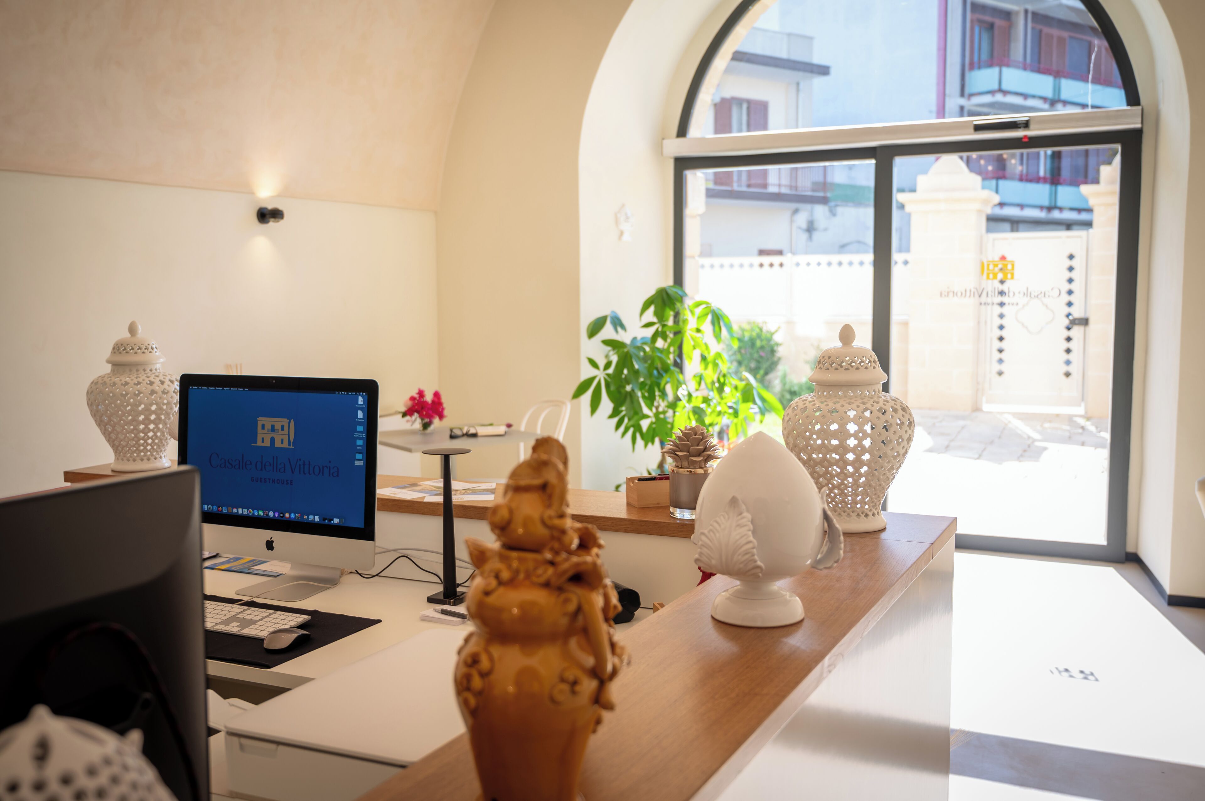 A reception desk with a computer, decorative items, and a view of the outside.