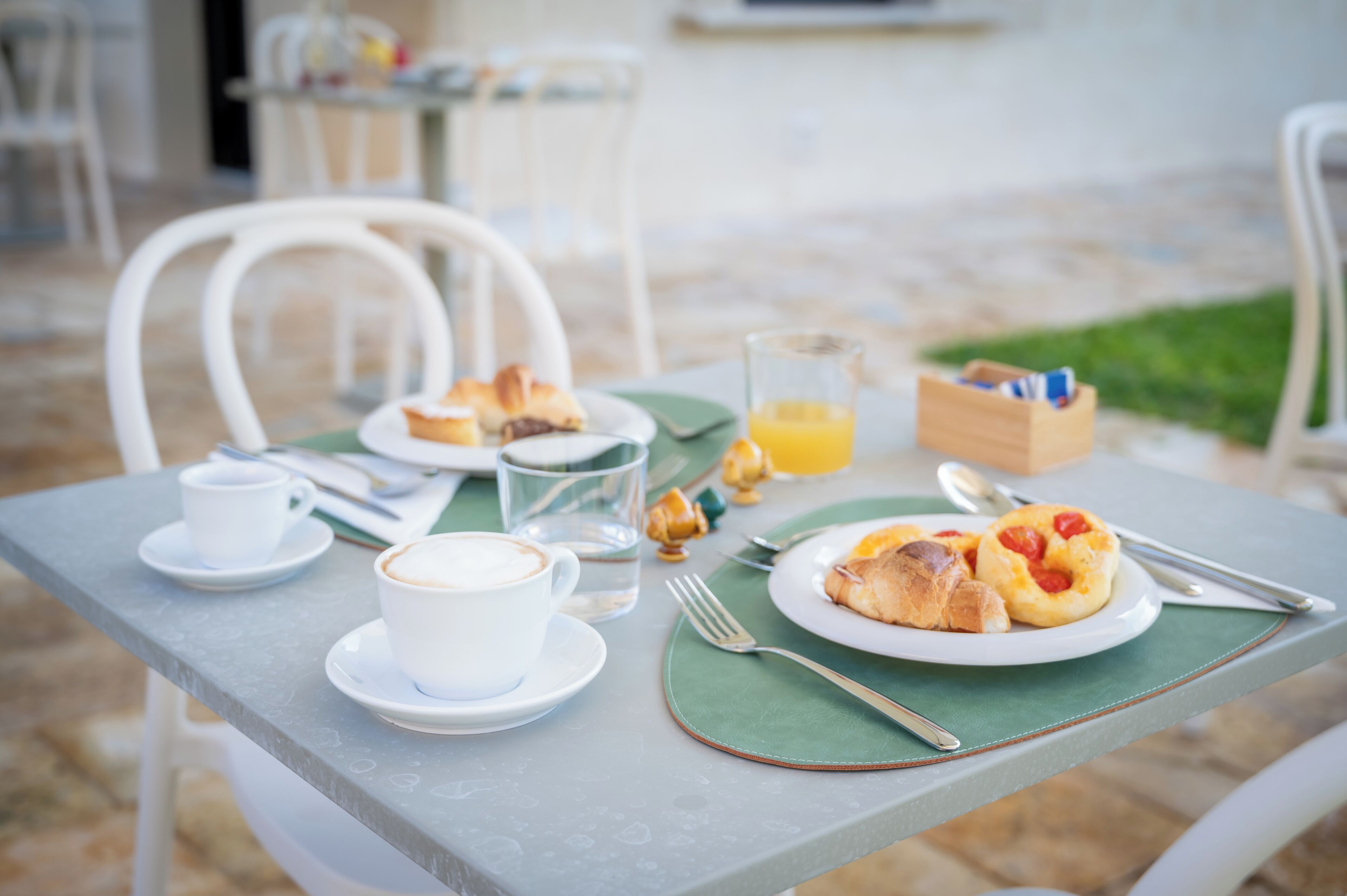 A breakfast table with a cup of coffee, a glass of orange juice, croissants, and a plate of pastries.