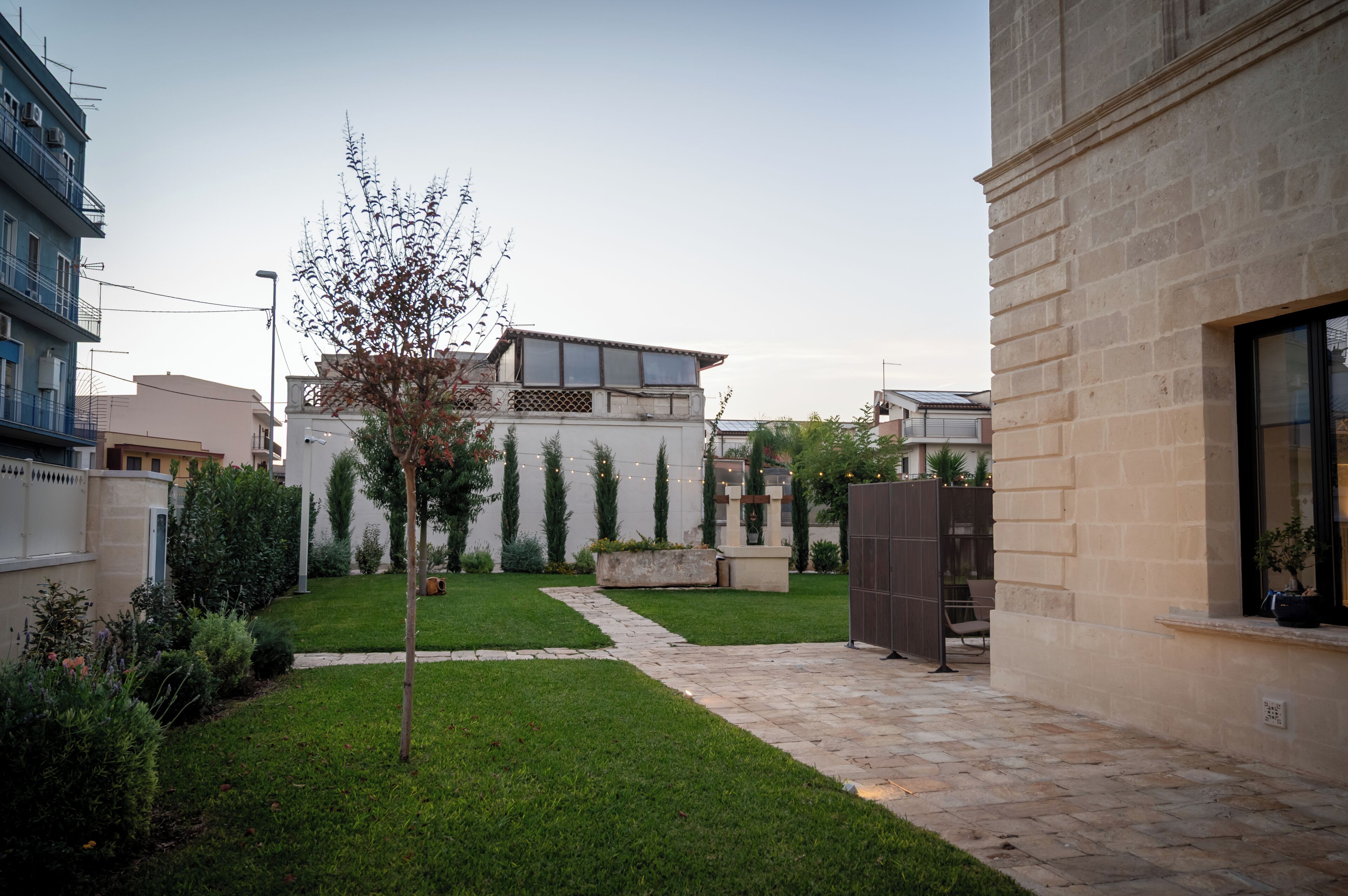 A courtyard with a pathway, a small tree, and a building with a stone facade.