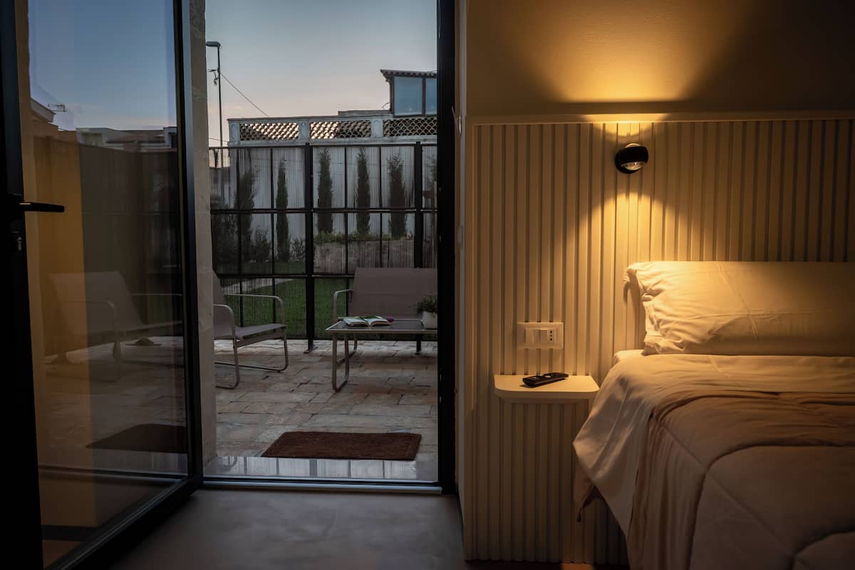 Una habitación de hotel con una cama, una mesita de noche y vistas al patio exterior.