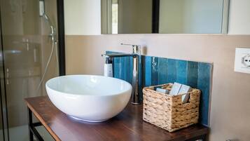 Un bagno con un lavabo bianco a forma di vaso, un rubinetto moderno, un cesto di vimini con articoli da toilette e uno specchio sopra il lavabo.