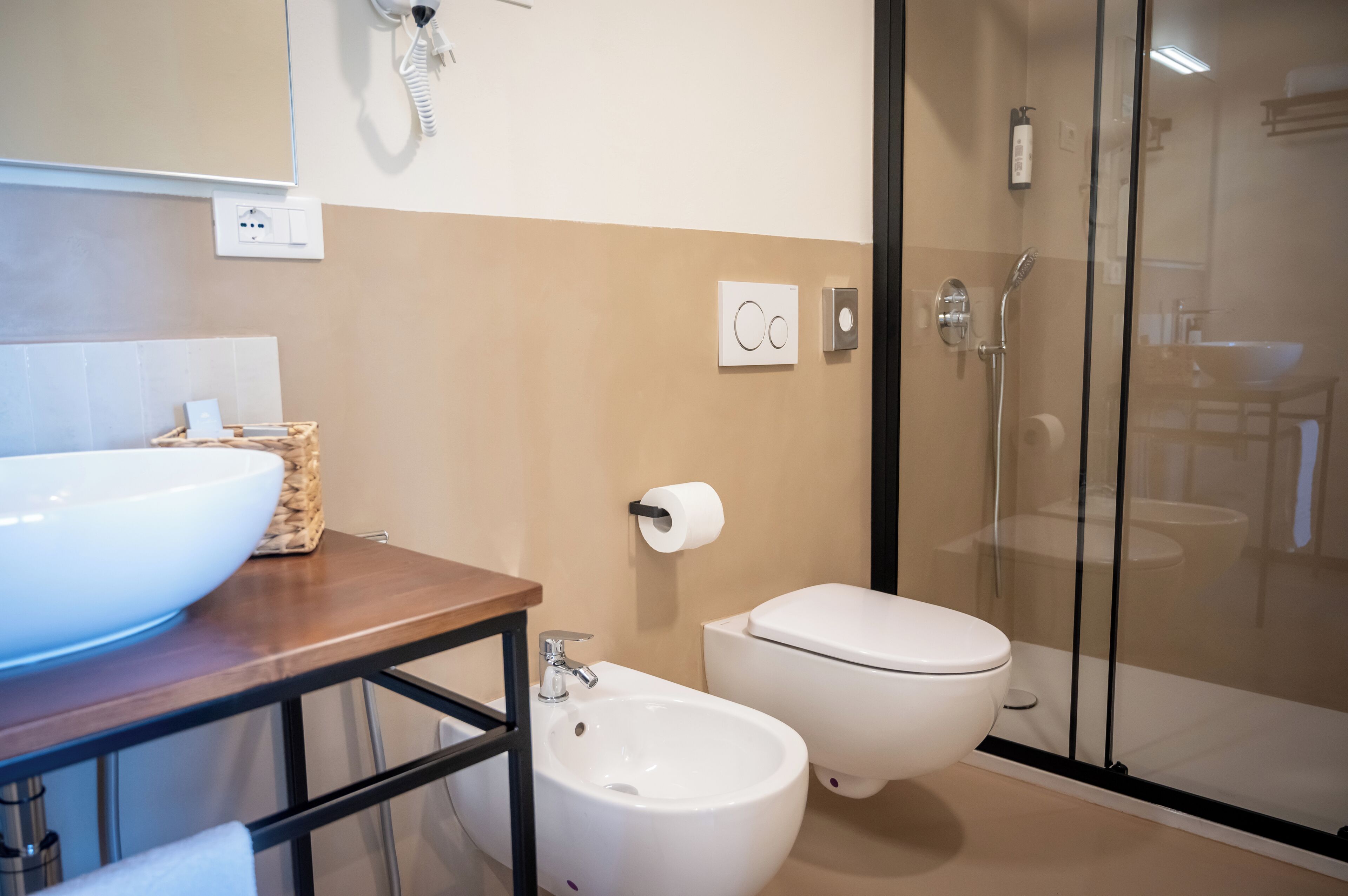 Un baño moderno con un lavamanos grande de color blanco, un bidé, un inodoro y una ducha con mampara de vidrio.