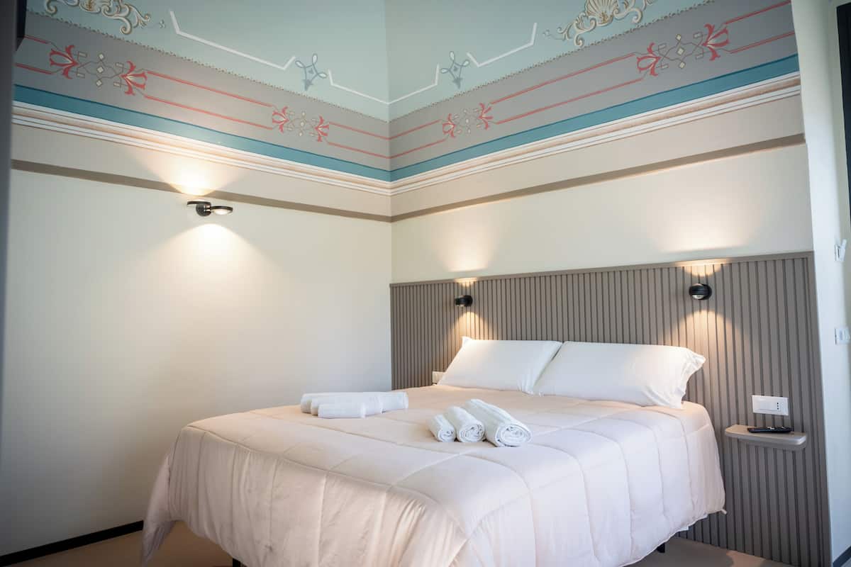 Una cama bien hecha con toallas enrolladas, una mesita de noche con un control remoto y paneles decorativos en la pared.