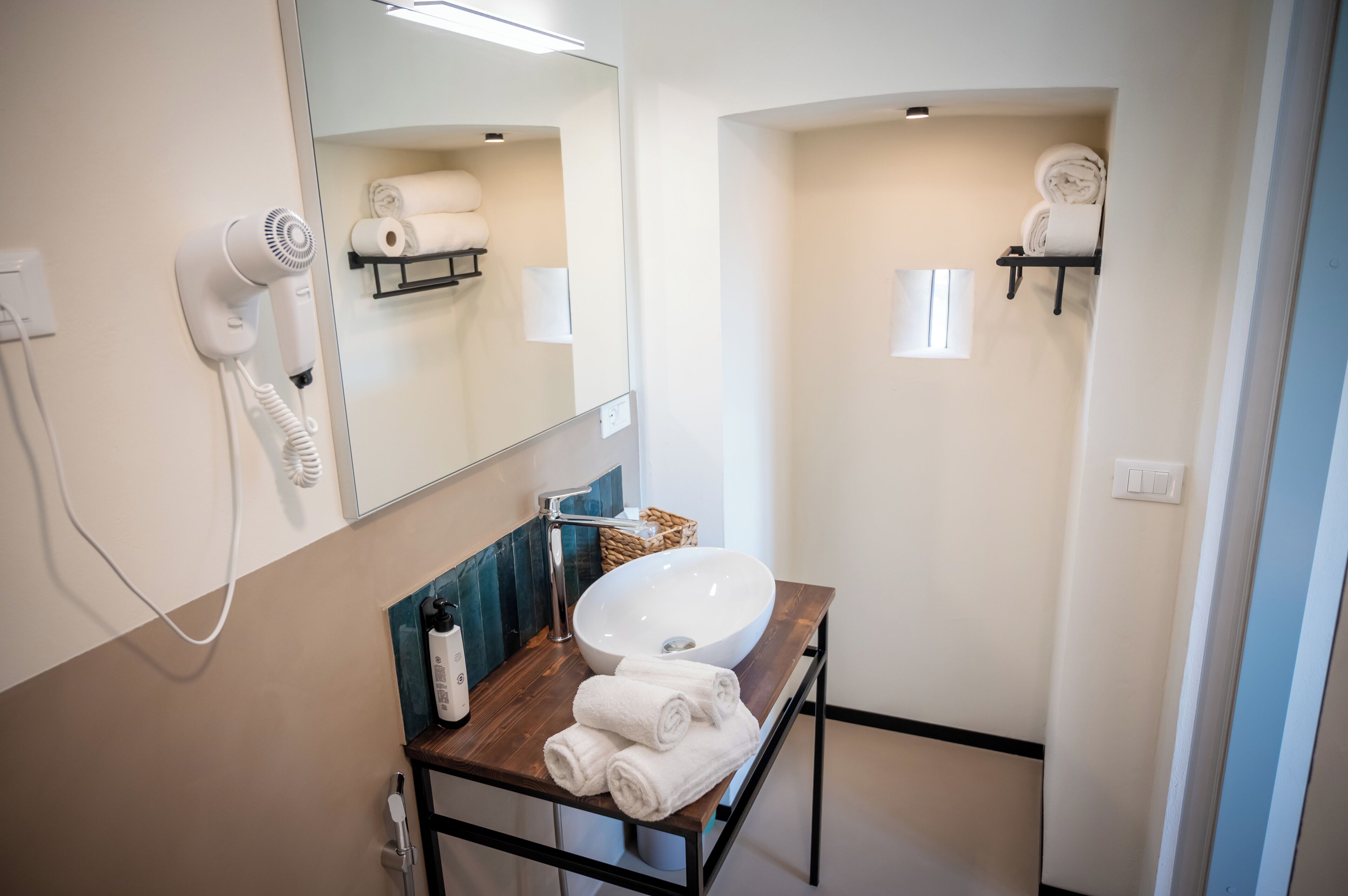 Ein modernes Badezimmer mit einem großen Spiegel, einem weißen Waschbecken und einem Haartrockner an der Wand.