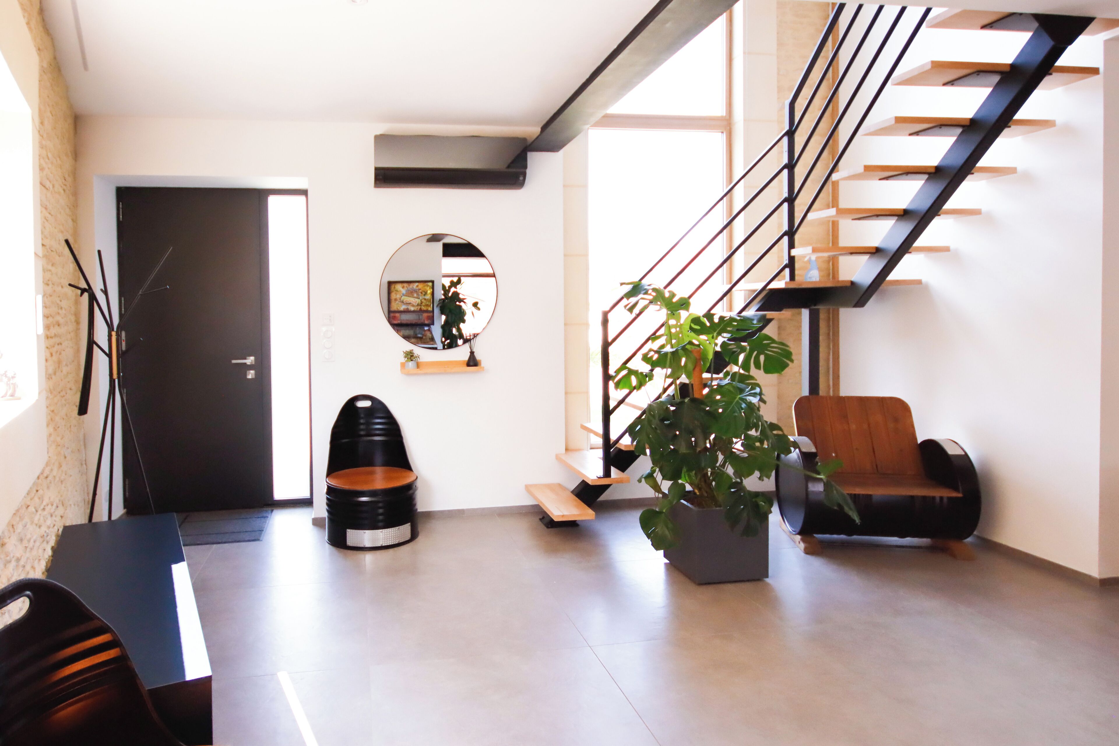 Una sala de estar moderna con una escalera, un espejo redondo, una planta en maceta y una silla de madera.