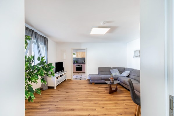 A modern living room with a sofa, TV, and a dining area in the background.