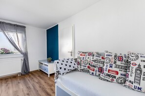 A bedroom with a bed, a bedside table, a window with curtains, and a view of the outside.