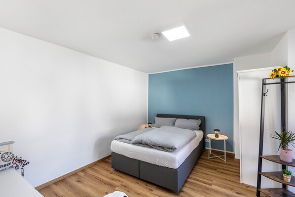 Een slaapkamer met een bed, nachtkastje en een klein krukje.