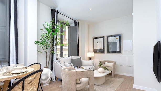 Ein modernes Wohnzimmer mit Essbereich, einem großen Fenster mit Vorhängen, einem Blumentopf und einem flachbildfernseher an der Wand.