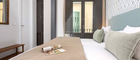 A hotel room with a large bed, a wooden bench, a mirror, and a view of the outside balcony.