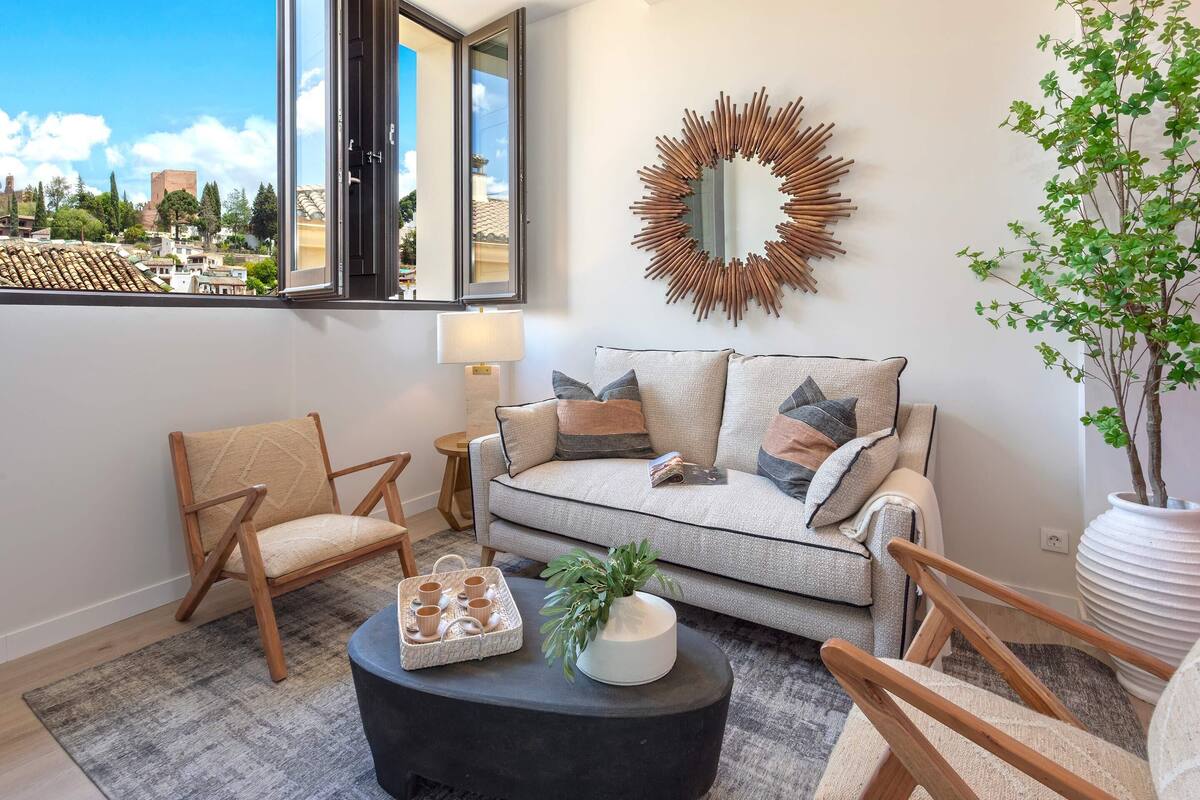 Un salon comprenant un canapé, des fauteuils, une table basse et une grande fenêtre donnant sur des immeubles.