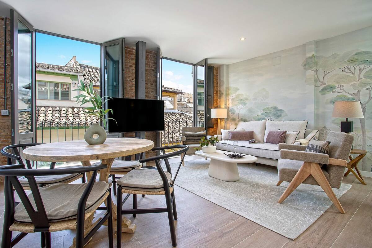 Un salon moderne avec une grande fenêtre, une table ronde en bois, un canapé et un téléviseur.