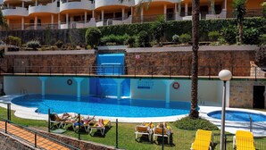 A hotel pool area with multiple lounge chairs and a small waterfall feature.