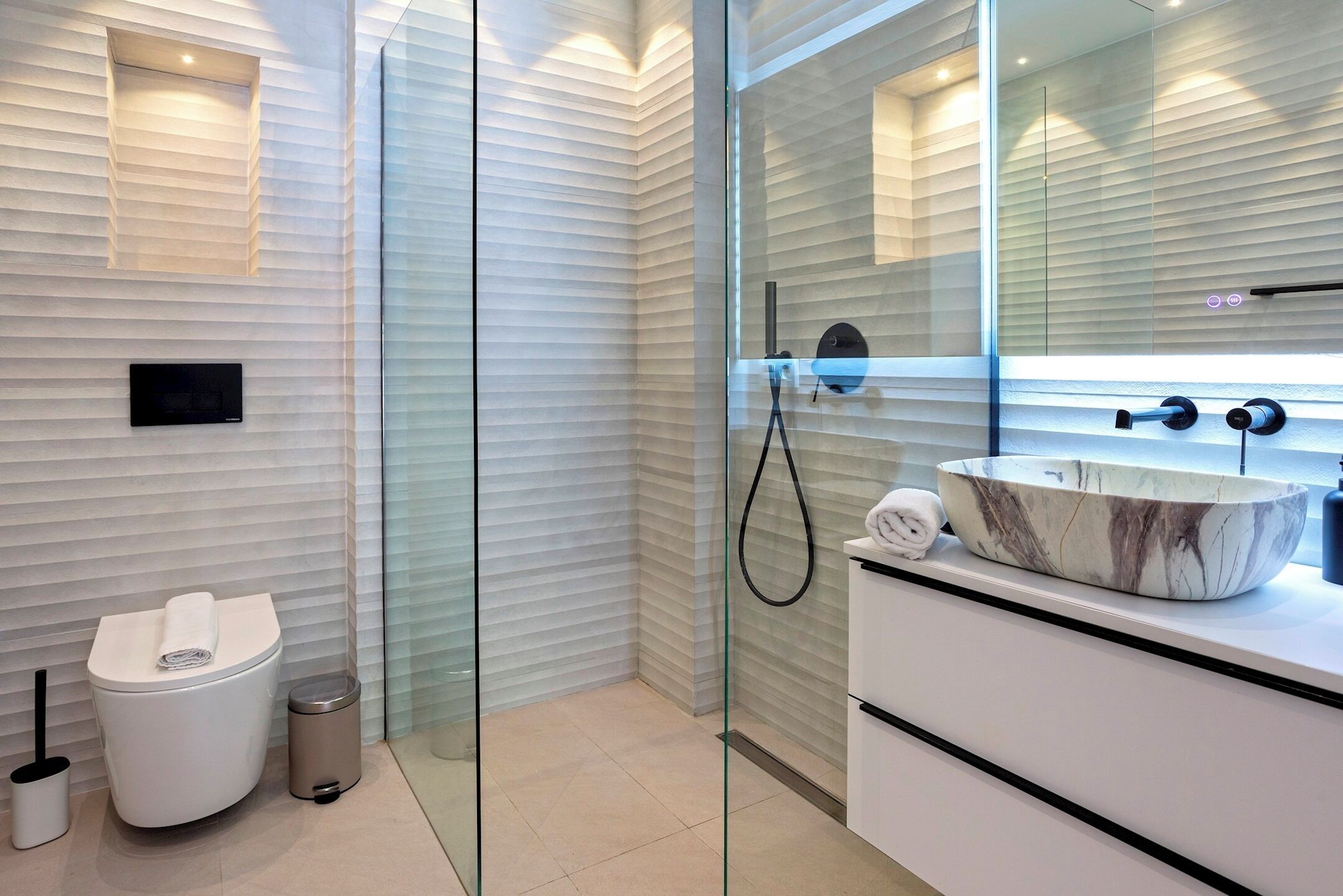 Un bagno moderno con box doccia in vetro, un water bianco, un lavabo in marmo e un piccolo cestino.