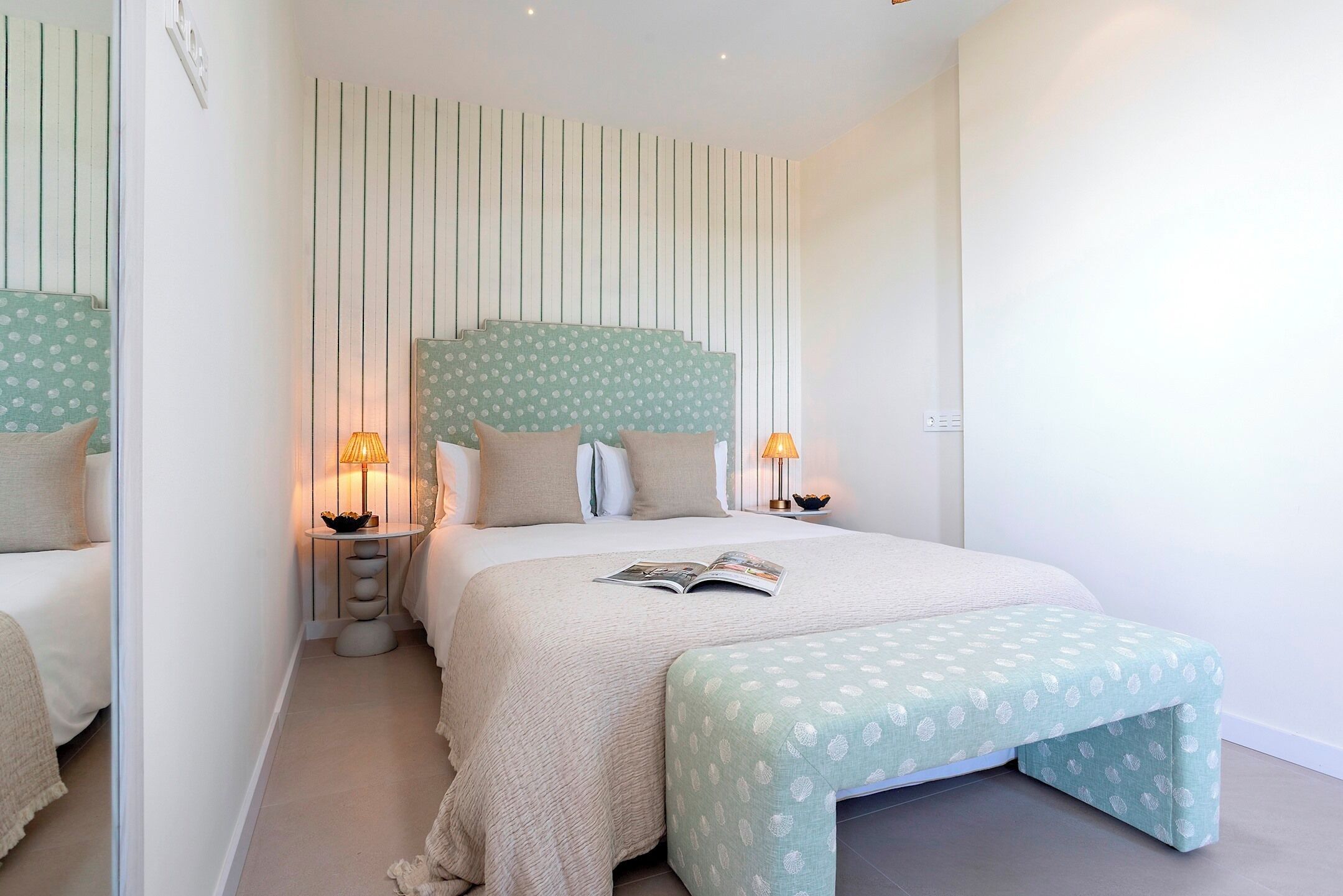 A bedroom with a bed, bedside lamps, a bedside table, and a bench.