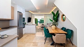 A modern kitchen with a built-in refrigerator, a dining area with a wooden table and green chairs, and a large potted plant. - Magnificent 3BD Duplex With Pool. Aloha Golf II (Marbella)