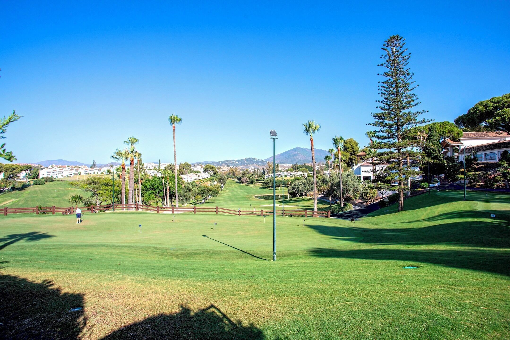 A golf course with a clear view of the green, a flagstick, and a distant mountain.