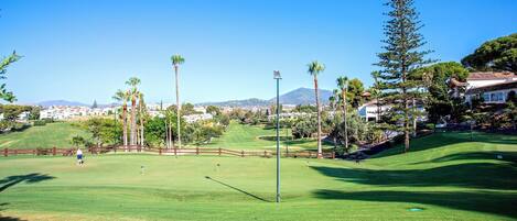 Un parcours de golf offrant une vue dégagée sur le green, avec un mât de drapeau et une montagne en arrière-plan.